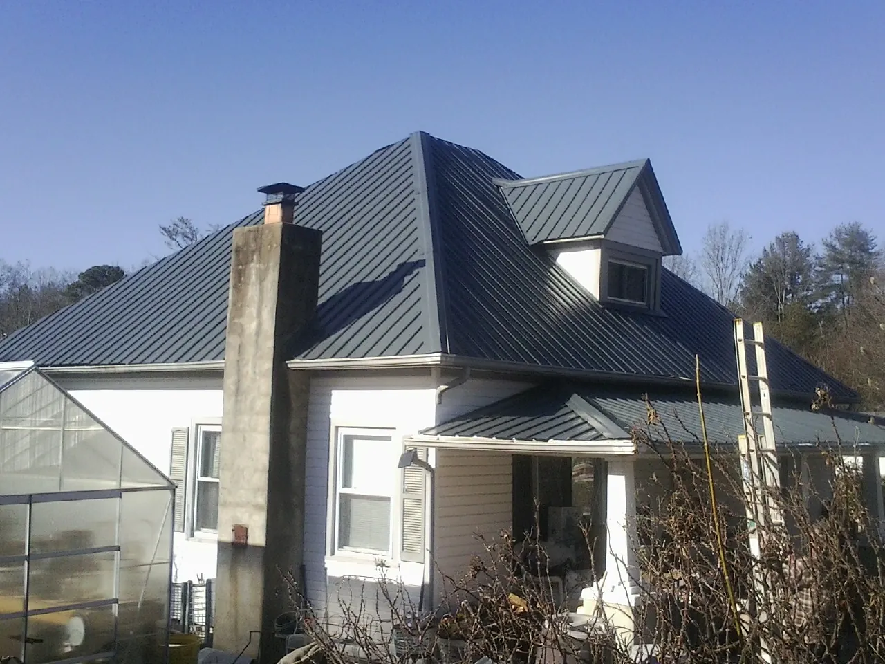 Dark blue standing seam metal roof on a white farmhouse with dormer — Slate & Tile Roof Repair by Roofing Brothers in Benzonia