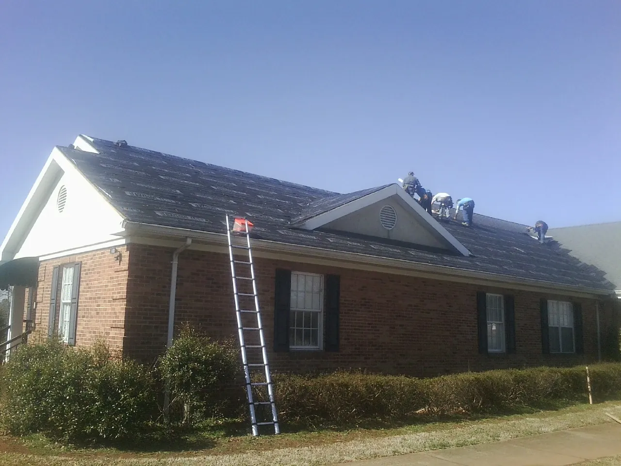 Crew tearing shingles off a brick ranch roof with a ladder set — Metal Roof Repair work by our crew in Benzonia