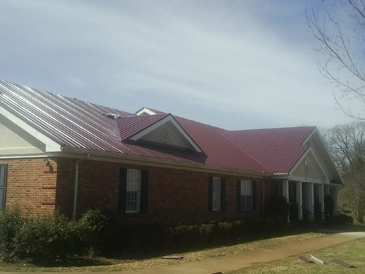 Red metal roof with gabled entries on a long brick building, from a Hail Damage Roof Repair job in Benzonia