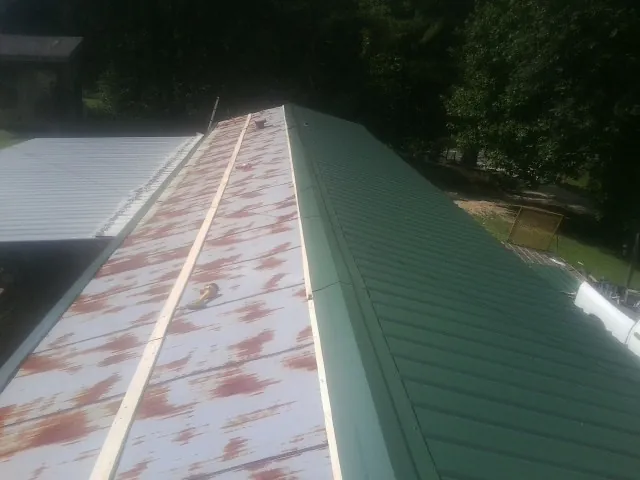 Old rusted panels beside newly installed green metal roofing — Wind Damage Roof Repair by Roofing Brothers in Benzonia