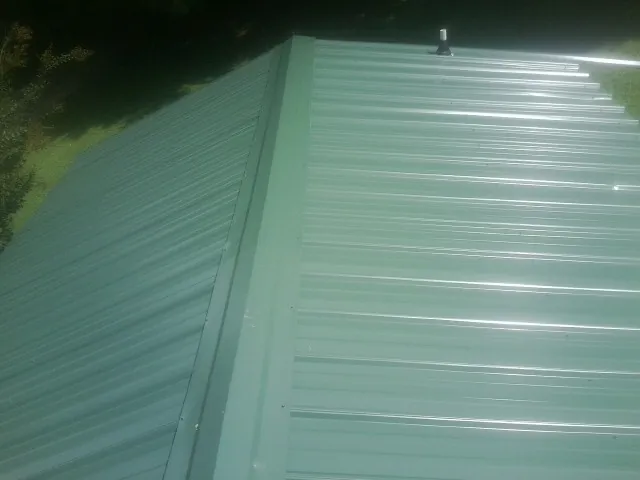 New green metal panels meeting at the ridge of a roof — Flat Roof Repair work by our crew in Benzonia