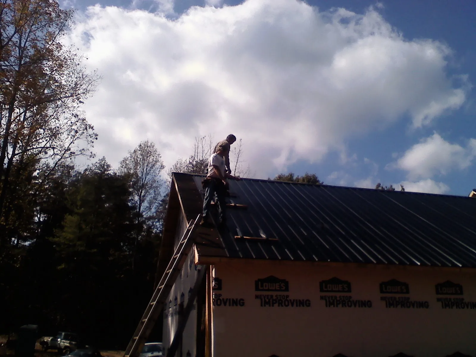 Roofer fastening dark metal panels high against a cloudy sky, from a Roof Inspection job in Benzonia