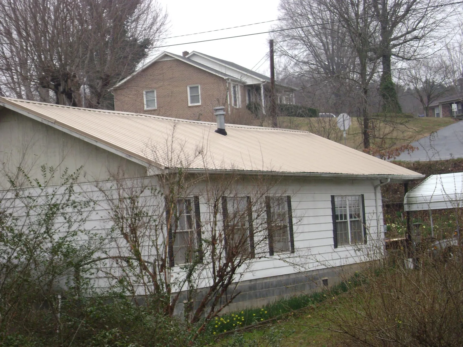 Tan metal roof on a white sided house set into a hillside — Commercial Roofing by Roofing Brothers in Benzonia