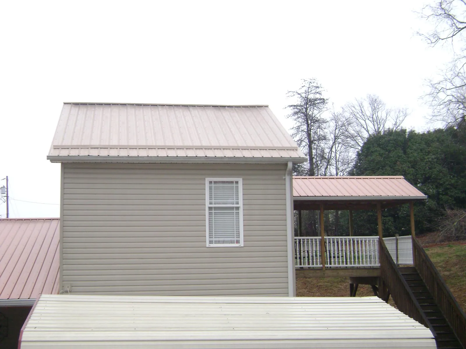 Tan metal roofs on a two story addition and attached porch, from a Roof Replacement job in Benzonia