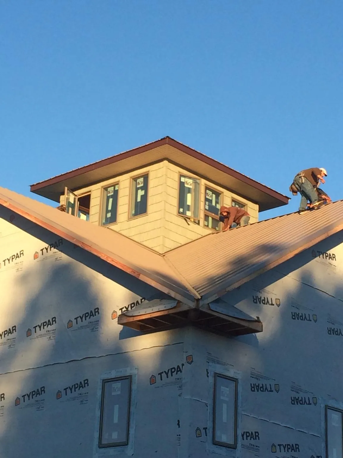 Roofers working around a rooftop cupola on a new metal roof at sunset — Roof Waterproofing in Benzonia by Roofing Brothers